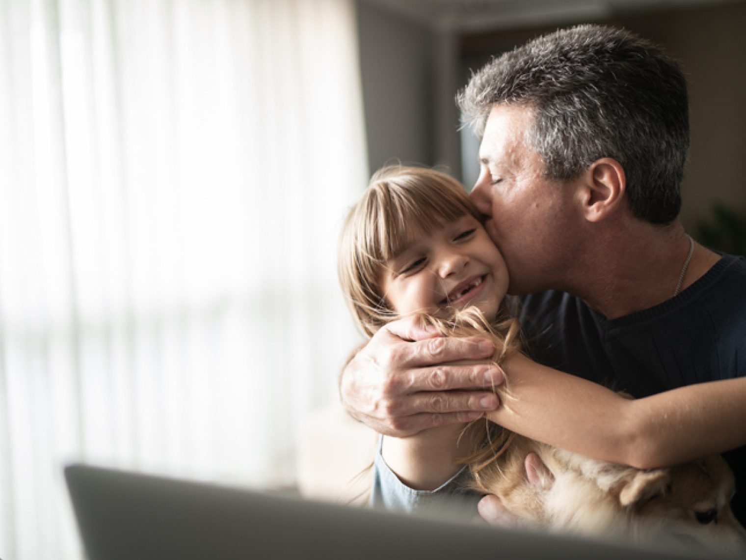 An affectionate moment of a father kissing his daughter on the cheek in their home.