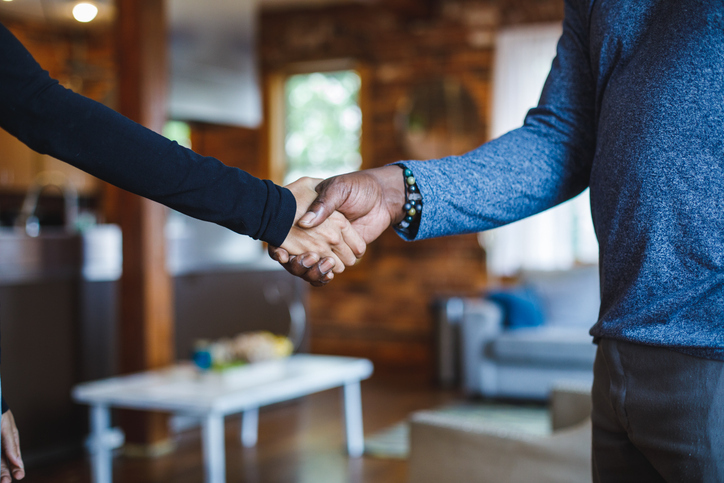 Two individuals in a home interior engage in a handshake, possibly finalizing a deal or agreement.