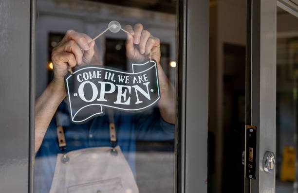 Hands Hang A Sign That Reads Come In, We Are Open On The Inside Of A Glass Door