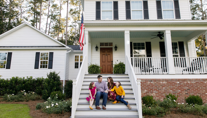 Family sitting outside on the steps of a new construction white siding farmhouse in the suburbs